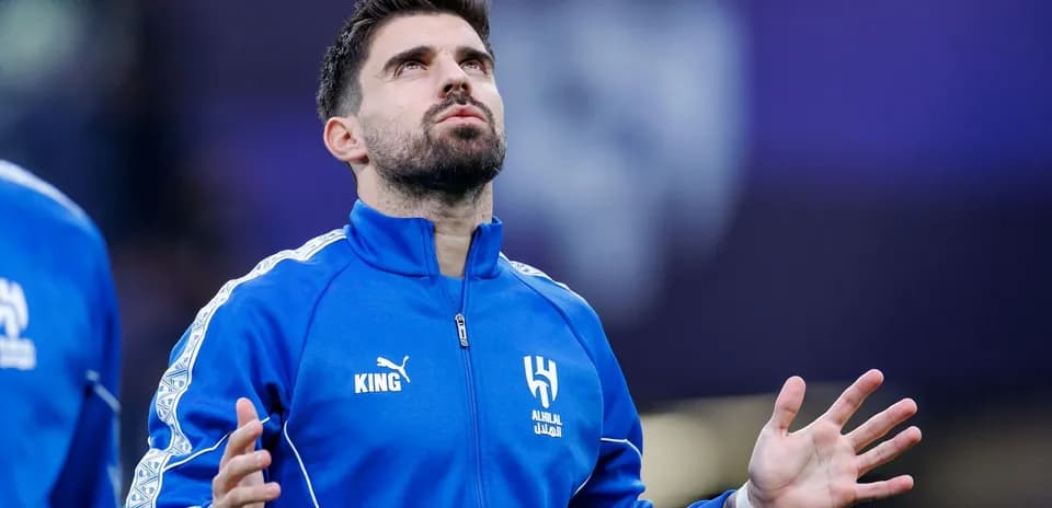 Player in blue tracksuit with arms raised during warm-up