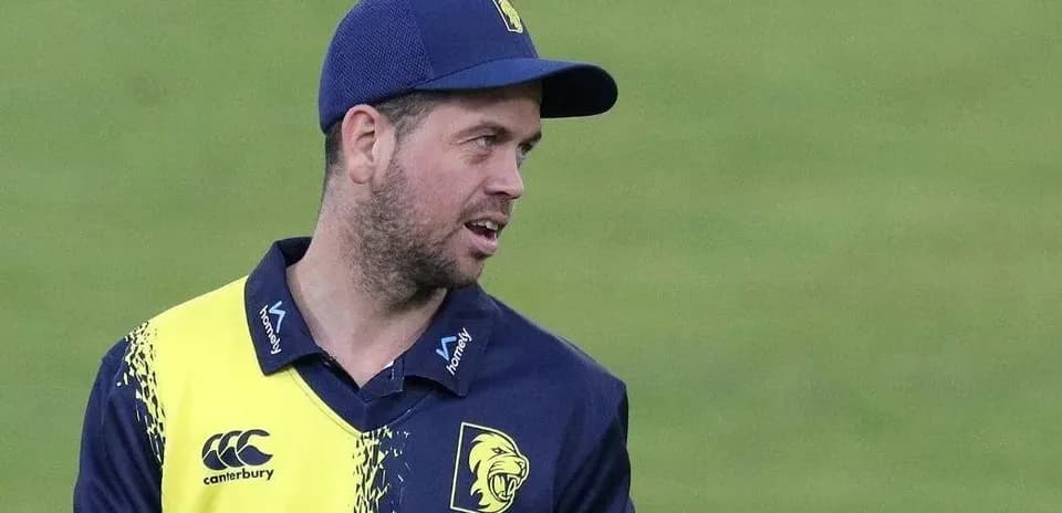 Cricketer in team uniform holding equipment on field