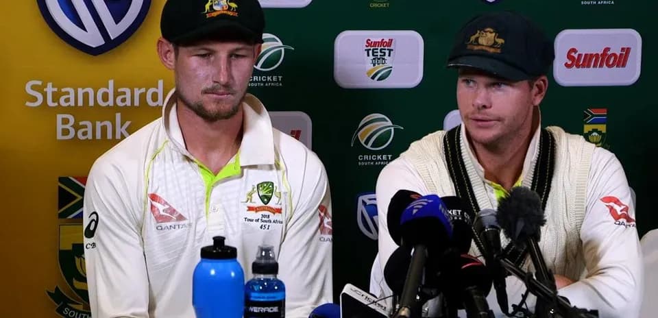 Two cricketers at press conference table with microphones