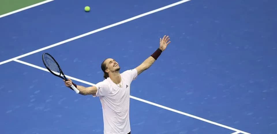 Tennis player celebrating on blue court with ball nearby