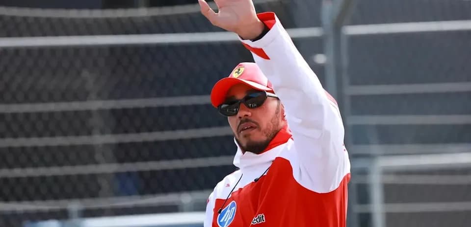 Driver waving while wearing racing gear and sunglasses