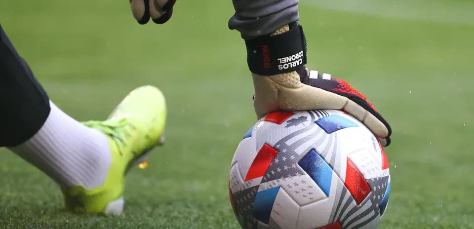 Goalkeeper placing hand on soccer ball on pitch