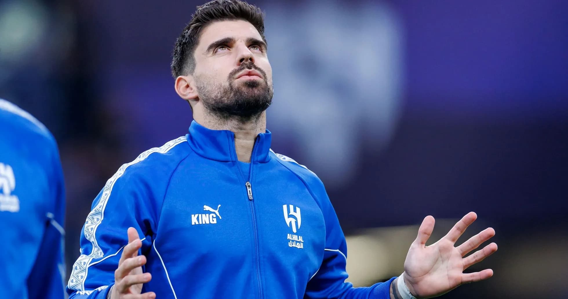 Player in blue tracksuit with arms raised during warm-up Player in blue tracksuit with arms raised during warm-up