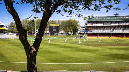 Cricket match in progress at stadium with trees Cricket match in progress at stadium with trees
