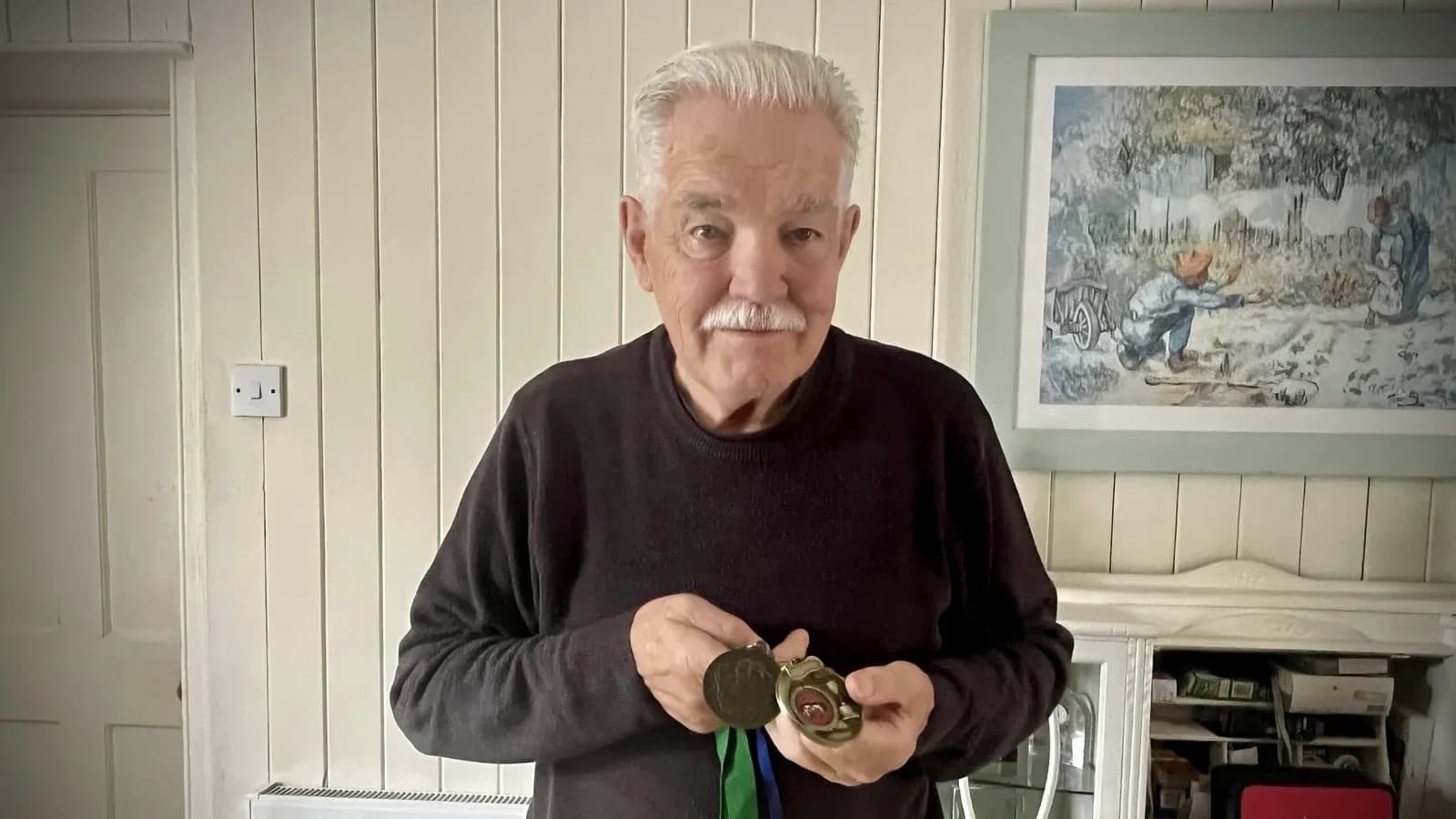 Elderly man holding medals in living room Elderly man holding medals in living room