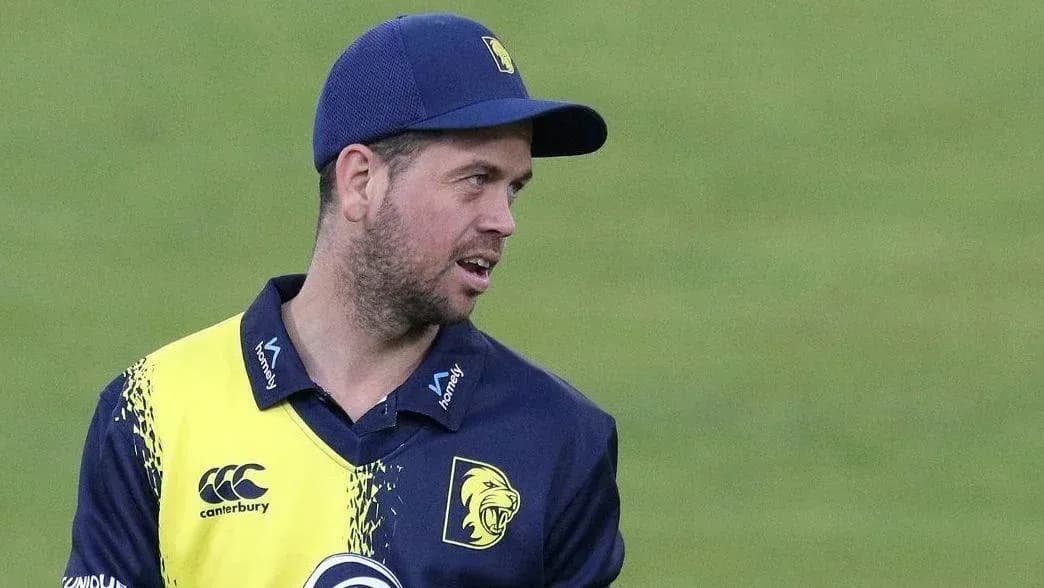 Cricketer in team uniform holding equipment on field Cricketer in team uniform holding equipment on field