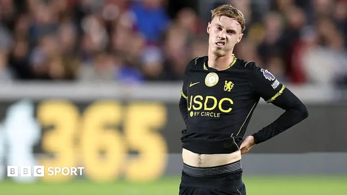 Player in black kit holding his stomach on field Player in black kit holding his stomach on field