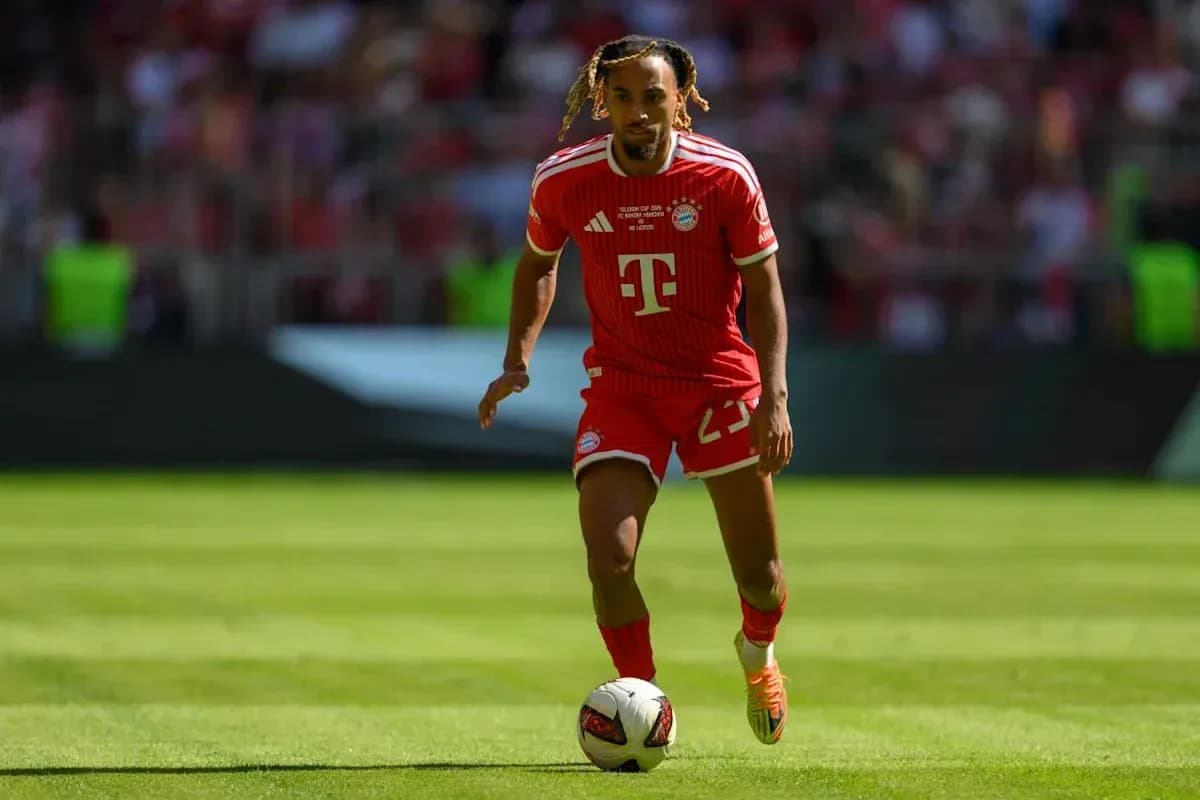 Player in Bayern Munich kit dribbling football on field Player in Bayern Munich kit dribbling football on field