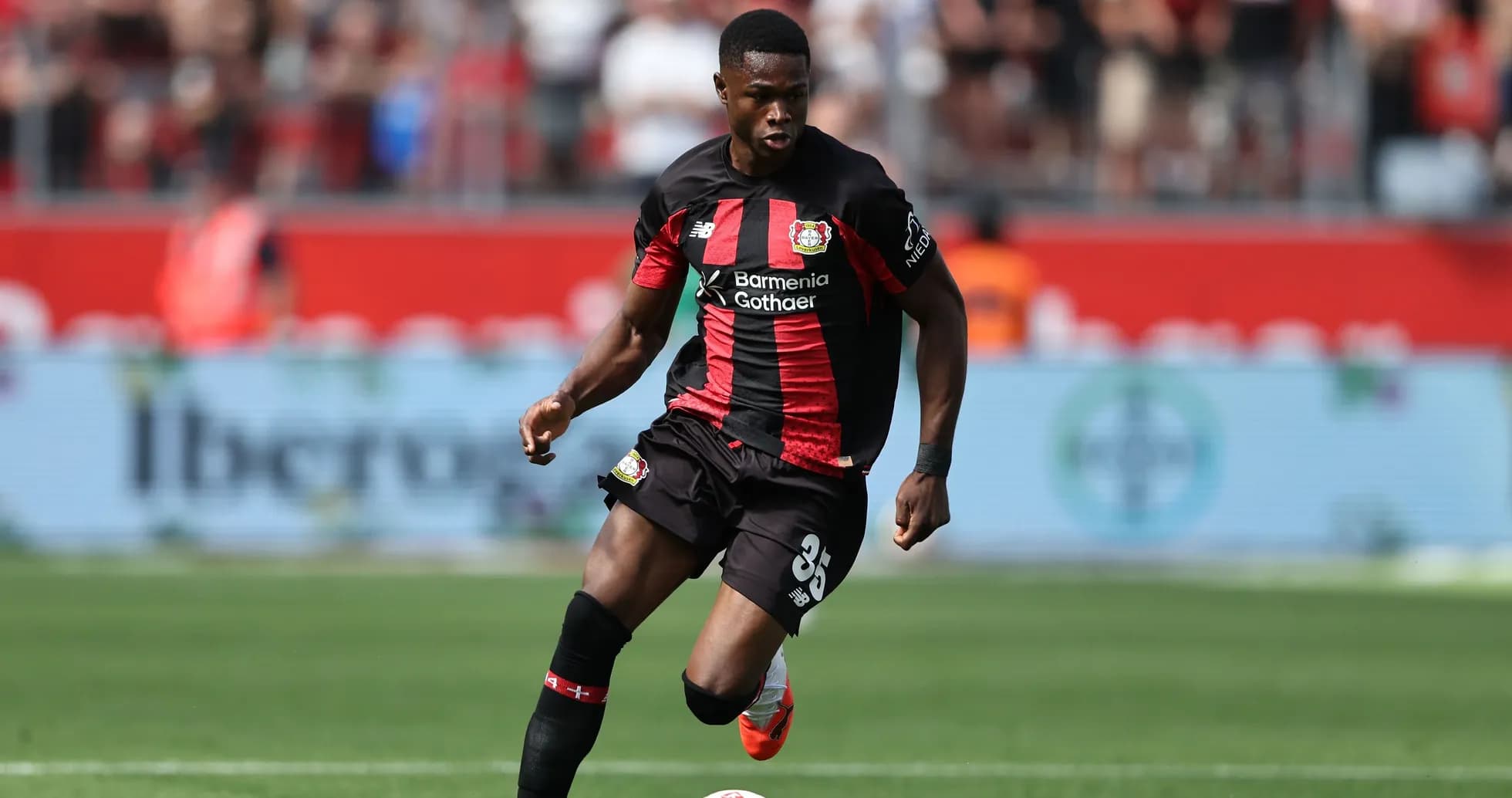 Player in black and red kit dribbling ball on pitch Player in black and red kit dribbling ball on pitch